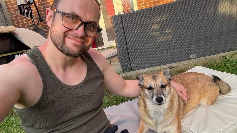 A Photo of myself, wearing a green vest, and my dog sat on a large cushion on the floor of a garden. 
